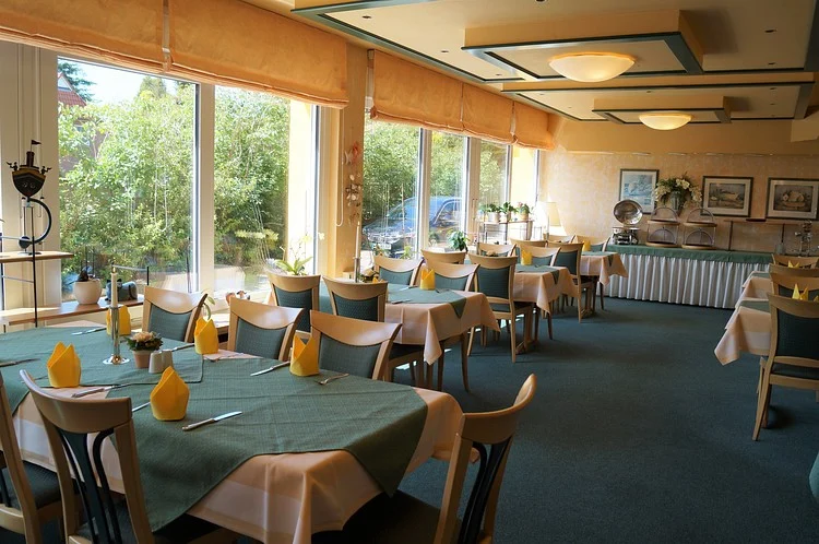 Der Gastraum des Restaurants mit gedeckten Tischen und großen Fenstern